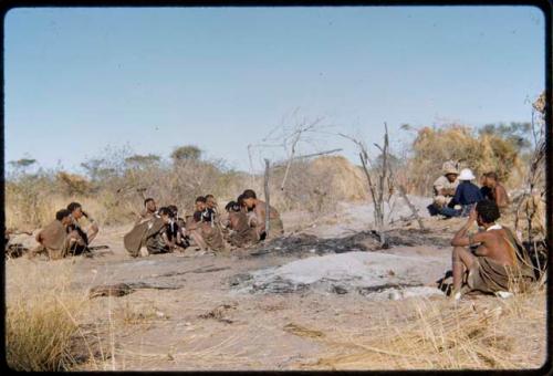 Fire, "Old ≠Toma's": People sitting near the remains of "Old ≠Toma's" skerm, burned to the ground, distant view with Kernel Ledimo and Lorna Marshall in the background