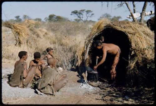 Food, Cooking: "/Qui Hunter" stirring food in a pot in front of a skerm, with his wife, /Naoka, and her mother, "Old /Gasa" sitting near him