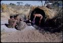 Food, Cooking: "/Qui Hunter" stirring food in a pot in front of a skerm, with his wife, /Naoka, and her mother, "Old /Gasa" sitting near him