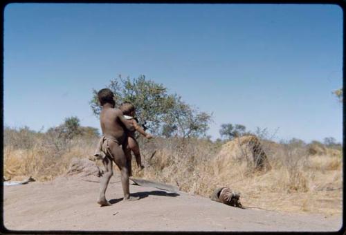 Children, Fathers and sons: Boy carrying a child across a termite mound, with another child rolling down the side of the termite mound