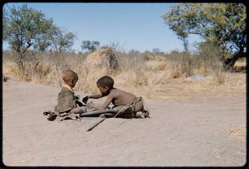 Children, Fathers and sons: /Gaishay (son of ≠Toma) working on a kaross, with !Ungka Norna sitting on it