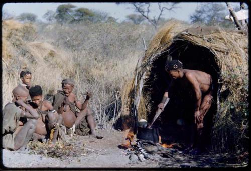 Food, Cooking: "/Qui Hunter" stirring food in a pot with a fire paddle, with his wife, /Naoka, her mother, "Old /Gasa," and an unidentified woman sitting near him