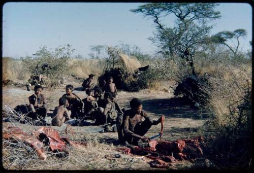 Food, Meat: "Gao Medicine" cutting up meat, with his family sitting behind him, including //Khuga (his daughter) in the middle