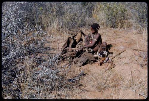 Food Gathering, Children: Bau of Band 10 sitting and holding up veldkos, with her child sitting on the ground next to her