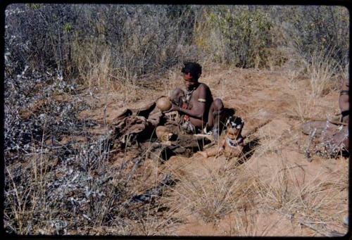 Food Gathering, Children: Bau of Band 10 sitting and holding up veldkos, with her child sitting on the ground next to her