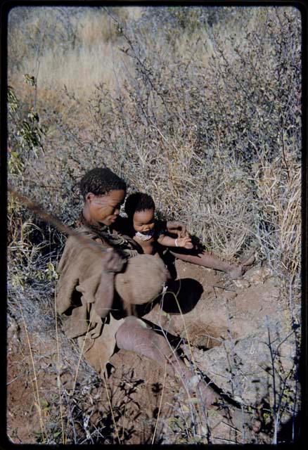 Food Gathering, Children: Woman holding a large root she has dug up, sitting with a child next to her, showing her scarification on her face