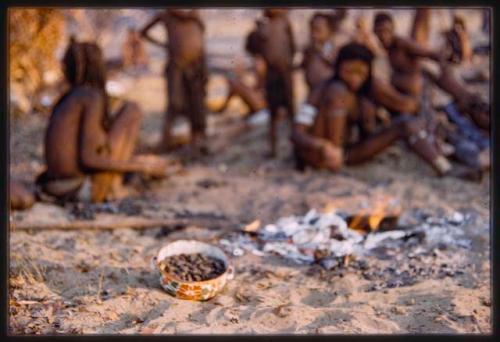 Group of people with bowl of food on the fire in the foreground (out of focus)