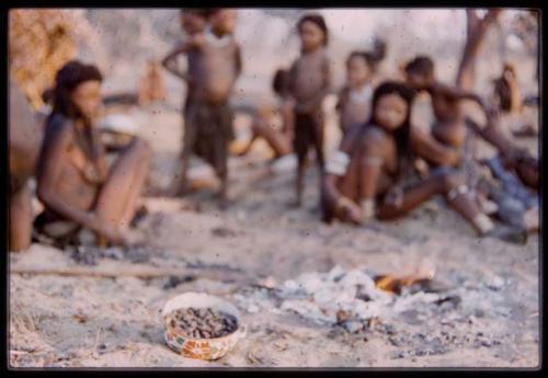 Group of people with bowl of food on the fire in the foreground (out of focus)