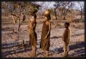 Two women carrying water on their heads and a boy, standing in the evening light