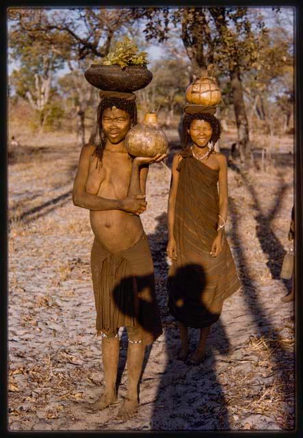 Two women carrying water on their heads, with Lorna Marshall in shadow