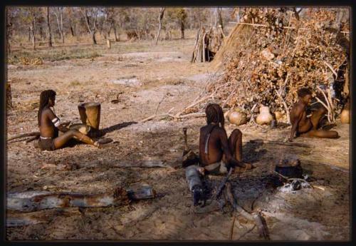 Woman sitting and sorting grain, with two other people on her right