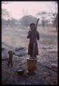 Woman standing with mortar and meal in a basket, with a baby standing next to her