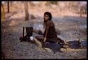 Girl cooking something in a pot, seated by fire (out of focus)