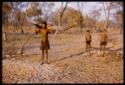Man carrying wood on his shoulders, with two boys standing on his side (out of focus)