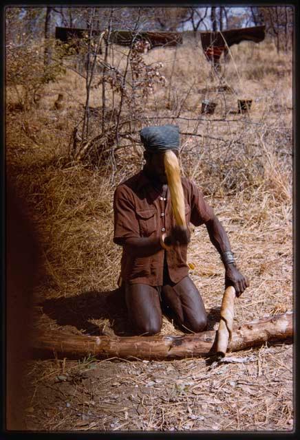 Bela, wearing a Western shirt, kneeling down and pounding hide