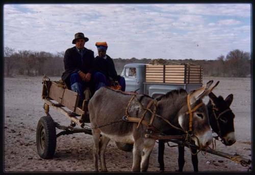 Two people riding a donkey cart, with Chevrolet in the background