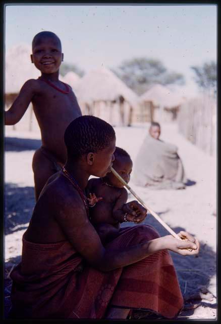 Woman playing a bow and holding a baby, with a boy standing near her