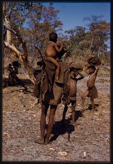 Man carrying a child on his shoulder standing next to two children