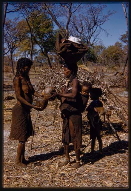 Woman with a child on her back pouring water for another woman