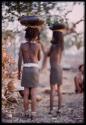 Two girls carrying bowls on their heads, seen from behind (image partially obscured)