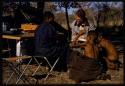 Nicholas England writing in a notebook, sitting with Kernel Ledimo, Hu/Na, and Kumsa