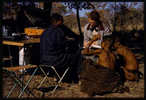 Nicholas England writing in a notebook, sitting with Kernel Ledimo, Hu/Na, and Kumsa