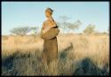 Grass: Woman standing, carrying a kaross full of grass used for bedding