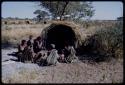 Groups: People sitting in front of Gau's skerm, including "/Qui Hunter" (inside the skerm), "Old Gau" squatting by the entrance, //Khuga (wife of !Naishi), /Naoka, "Old /Gasa" with shaved head, /Qui (son of Gau and Khuan//a), and Be (Gau's first wife)