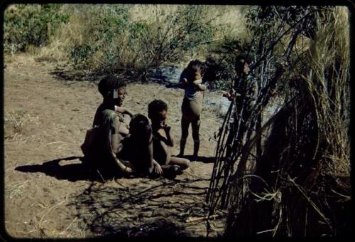 Groups: N!ai sitting, with several children sitting and standing next to her