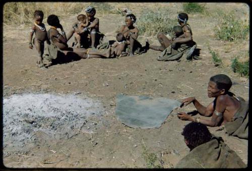 Groups: Group of people sitting around the ashes of "Gao Medicine's" fire, including Khwo//o (right), !U wearing ornaments, !Ungka (≠Toma's sister), Be and Khuan//a