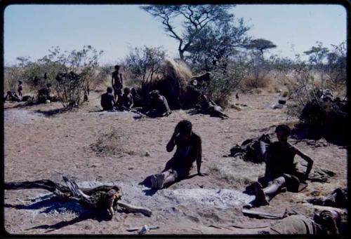 Groups, Extended Family: ≠Toma and /Naoka (wife of "Gao Medicine") sitting, with a group of people sitting next to a skerm in the background