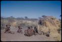 Groups, Extended Family: "Old /Gam" sitting with ≠Nisa, /Gasa holding a baby and /Naoka holding Khuan//a (≠Nisa's child) in front of Gau's skerm, with a kudu head on the ground next to the skerm