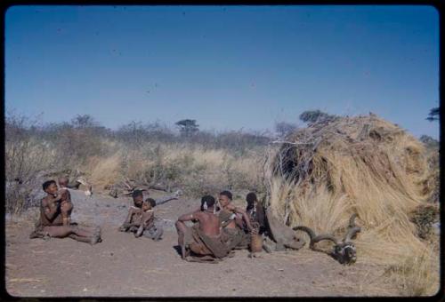 Groups, Extended Family: "Old /Gam" sitting with ≠Nisa, /Gasa holding a baby and /Naoka holding Khuan//a (≠Nisa's child) in front of Gau's skerm, with a kudu head on the ground next to the skerm