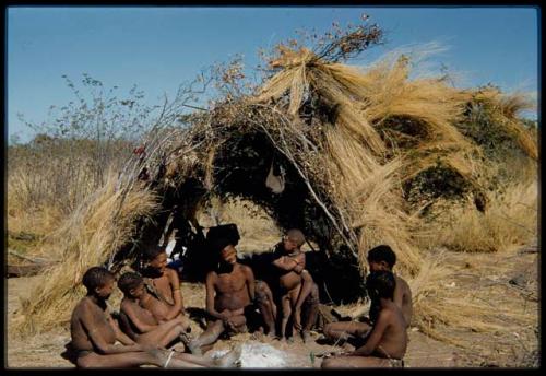 Groups, Extended Family: Gau's family sitting in front of a skerm (left to right): ≠Toma, !Naishi, Be their mother, Gau, /Qui held by Khuan//a (Gau's second wife), /Gunda (husband of N!ai and son of Khuan//a by a former marriage with Bo) and ≠Gao (son of Gau and Be)