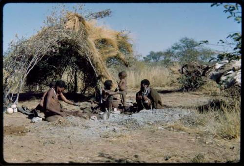 Groups, Extended Family: Be and Khuan//a (wives of Gau) sitting with /Gam in front of a skerm, with a child standing next to them