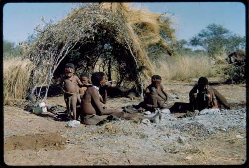 Groups, Extended Family: Be and Khuan//a (wives of Gau) sitting with /Gam in front of a skerm, with a child standing next to them