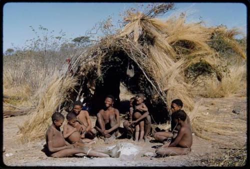 Groups, Extended Family: Gau's family sitting in front of a skerm (left to right): ≠Toma, !Naishi, Be their mother, Gau, /Qui held by Khuan//a (Gau's second wife), /Gunda (husband of N!ai and son of Khuan//a by a former marriage with Bo) and ≠Gao (son of Gau and Be)