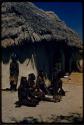 Group of women sitting and one standing next to a hut at William Hartley's waterhole