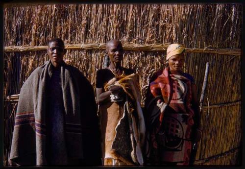 Three women standing against a hut