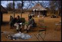 Lorna Marshall and Kernel Ledimo sitting in a chair at a campsite; Lorna is taking notes