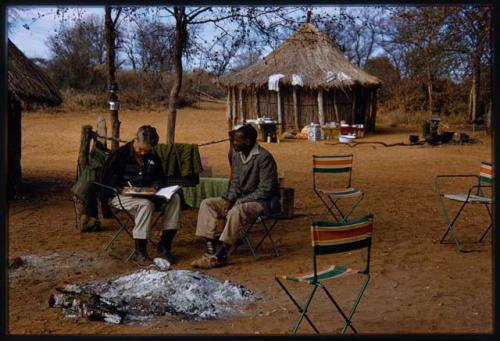 Lorna Marshall and Kernel Ledimo sitting in a chair at a campsite; Lorna is taking notes