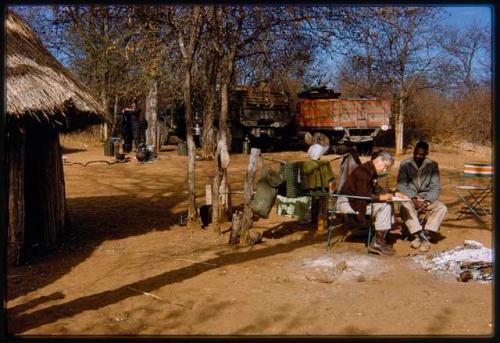 Lorna Marshall and Kernel Ledimo sitting in a chair at a campsite; Lorna is taking notes