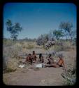 Group of men sitting together; one working with mortar and pestle