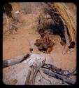 Woman cooking food in can, squatting in front of a skerm