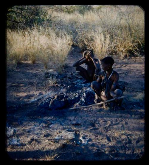 Two women cooking animal head in ashes