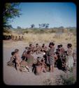 Circle of women with boys wearing dance rattles, gathered for a curing dance, with someone being deloused