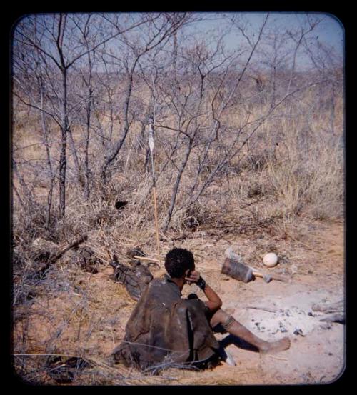 Woman sitting by ashes of fire, seen from a distance