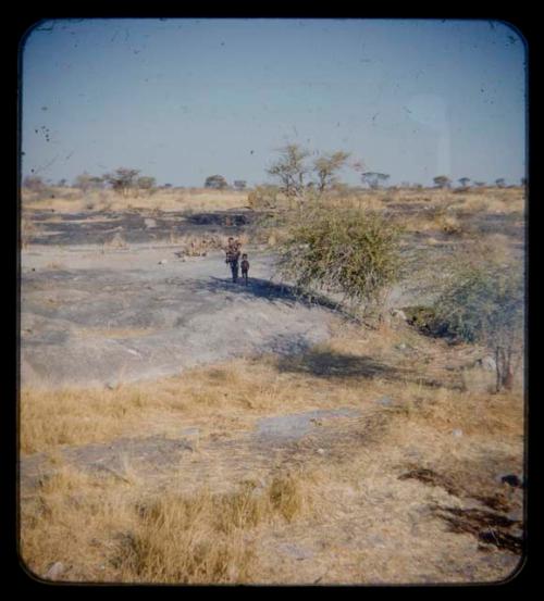 Person holding a baby and one child, standing by burned area