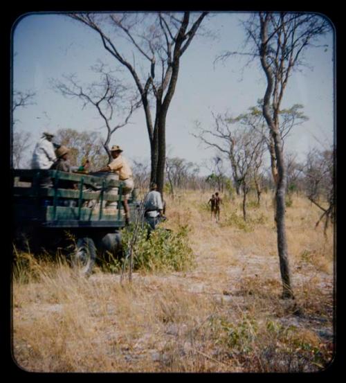 Expedition members in a truck, with two men walking ahead of them