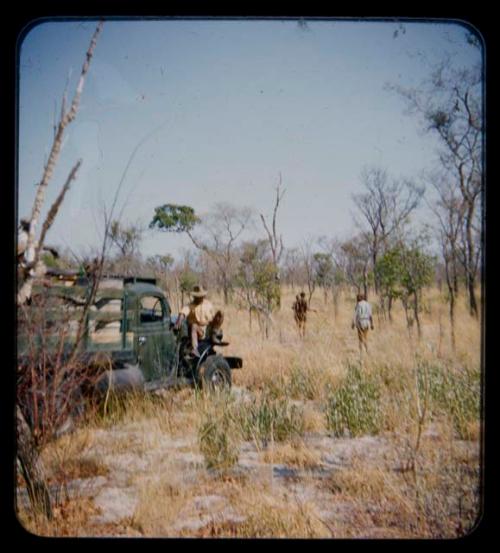 Expedition members in a truck, with two men walking ahead of them